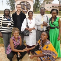 Suzan Kirima, Nkatha Murungi, Mercy Mugure, Felician Mkude, Tiba Kaihuzi, Chris Lytle, and Nancy Amwoso Aswani pose outside in front of the genocide memorial.