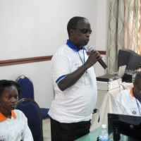 Kinubi Francis speaks into a microphone with other participants seated around him.