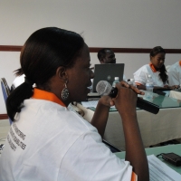 Gloria Namureme speaks into a microphone. Other participants are seated in the background.