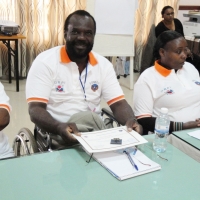 Tambo Camara is at a table alongside other participants. His certificate is on the table in front of him.