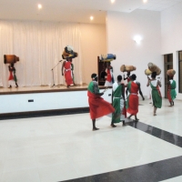 A line of drummers carrying drums walks onto a stage in a large white room