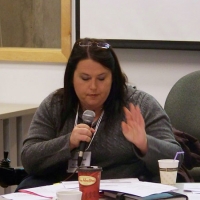 Susan Ralph is speaking into a microphone while looking down at a paper.