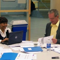 Two participants smile while working at a table littered with meeting papers.
