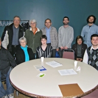 A group photo of the participants in the training seminar who are all standing behind a round table.