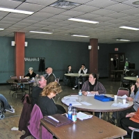 <p>
	Training participants sit around tables listening to Norman Boucher speak.</p>
