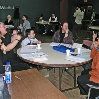 A group of training participants are talking while seated around a table. Other participants can be seen in the background.