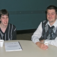 Lyne Robichaud and Jean-Michel Bernier sit at a table and smile while drinking coffee out of styrofoam cups.