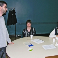 Simon Toulet stands while speaking with Lyne Robichaud and Jean-Michel Bernier (both seated at a table).