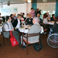 Training participants are seated around small tables. Video cameras on tripods can be seen in the background.