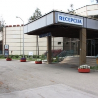 The entrance to the hotel is shown. A paved road leads up to the entrance over which a sign reads 'Recepcija'.