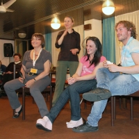 <p>
	Three participants (two females and one male) are seated in chairs and one woman is holding a microphone. A sign language interpreter stands behind them and signs.</p>
