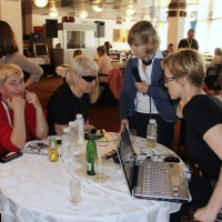 <p>
	Three women sit around a small table with many beverage bottles, headsets and a laptop computer. Marcia Rioux stands beside the table with a microphone.</p>
