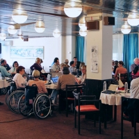 Many participants are arranged around tables in the training room.