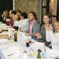 Participants sit at a long table, smiling and clapping their hands during dinner at Novi Kneževac. 