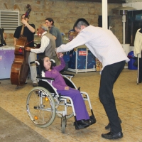 A young man and a young girl in a wheel chair smile and dance together.