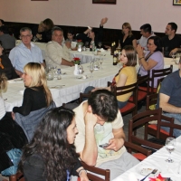 Participants are seated beside long tables with  white tablecoths, wine glasses and water pitchers. Some are clapping.