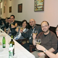 Participants and organizers sit at long tables and raise their wine glasses while smiling for the photo.