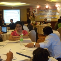 Nathan Bond stands and Marcia Rioux sits in the background while participants listen and work with training materials in the foreground. 