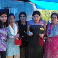 <p>Five women from stand outside beneath a blue tarp with crafts they created.</p>
