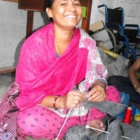 <p>Woman from Entire Power in Social Action, a disabled women&#39;s organization, sitting crossed legged working on a knitting project and smiling at the camera.</p>
