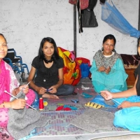 <p>Four women from Entire Power in Social Action sitting in a semi circle on the ground working on crafts and smiling</p>
