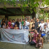 <p>People pose around a large white banner full of writing and drawings. Most people are holding up a single finger in the air.</p>

