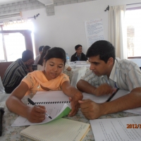 <p>
	Two participants are sitting inside the training room as they point to a page in their training manuals with other training items on their table including note books and a microphone.</p>
