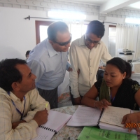 Ram is assisting with a discussion held by Mr. Birendra and two participants. Ram and Mr. Birendra are standing and the other two participants are seated. 