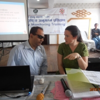 Mr. Birendra (left) and Rita Samson (right) sit as Rita makes a point with her arm raised to point at the computer in front of them. They are facing each other. 