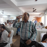 A participant stands as he adds to the discussion. He holds a micro phone in his right hand and he is holding it to his mouth. 