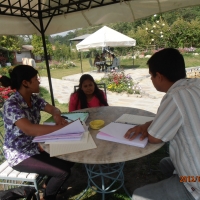 <p>
	A table outside in the garden, with three people seated at the table. There are training materials on the table and all three people are facing each other.</p>
