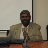 <p>
	Jace Nair is sitting at a table, speaking into a microphone.</p>
