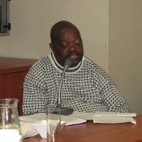 Muzi Nkosi is sitting at a table, speaking into a microphone. 