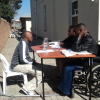 Lubabalo Mbeki is siting in front of Muntezihlupha Sibiya Wiseman and Sibusiso Sithole at a table outside of the training venue.