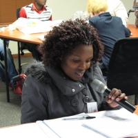 Bethulisile Zinyane holds a microphone during the session, while seated at a table looking down at her papers. 