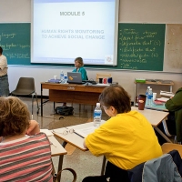 Steve Estey is speaking near the front of the room while participants sit at small desks and listen.