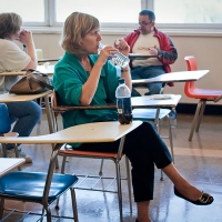 Marcia Rioux is seated at a desk and drinking water from a plastic water bottle.