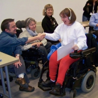 Participant Robin smiles broadly while holding a certificate and shaking hands with Steve Estey.