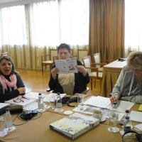 Three participants are gathered around a table, one participant looks down at her notes.