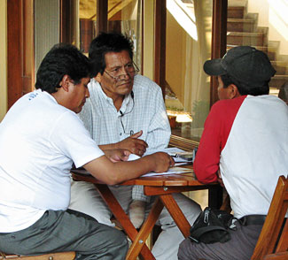 Three male training participants are seated around a wooden table while practicing interviews.