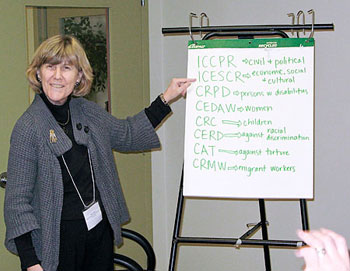 Marcia Rioux smiles while pointing to a large easel displaying acronyms of U.N. conventions