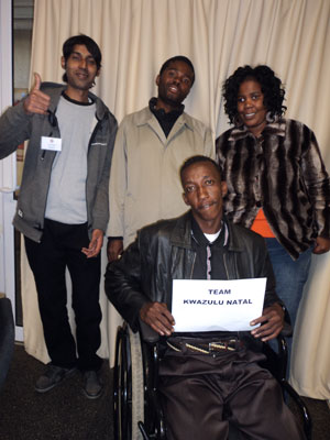 Site Coordinator (woman) and three monitors (all men) are posing for a group picture, holding a sign that says “Kwazulu Natal”. One of the monitors is making a ‘thumbs up’ sign.