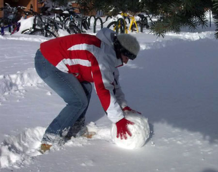 A picture of a person rolling a snowball outside during winter